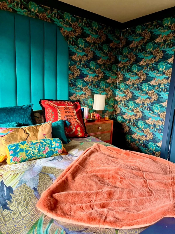 eclectic blue bedroom with print wallpaper and orange throw